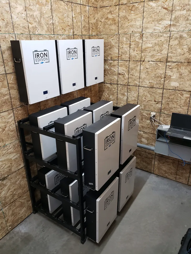 White lithium battery modules stacked on a black rack beside wall-mounted inverters