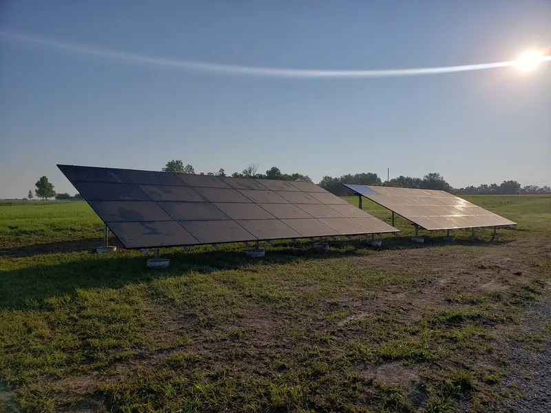 Two ground-mounted solar arrays in an open field at sunset