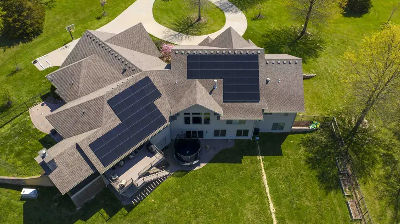 Aerial view of a large home with several rooftop solar arrays surrounded by green lawn